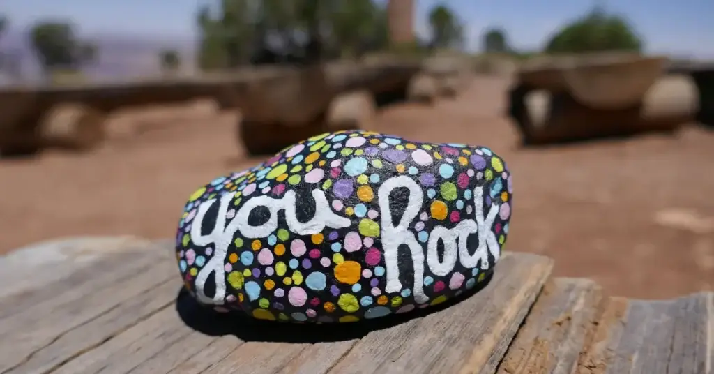 hand painted rock that says you rock on it in cursive surrounded by dots